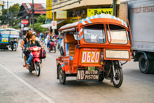 Negros Oriental, Asia - June 19, 2018: Negros Oriental  showing cars tricycles and two wheeled motorcycles with passengers on the street in the Dumaguete area with people on the background