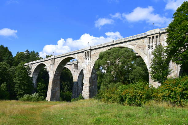 istock Two large brick and concrete railway bridges seen from below with trees surrounding them and some white puffy clouds visible on the summer sky seen during one of travels around Poland 1010534410