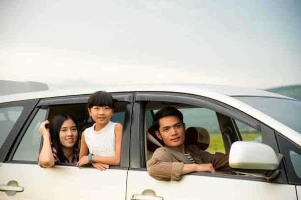 drive in the vacations family; asian family are happy sitting in the open trunk of a car;  travel nature trip. stock photo