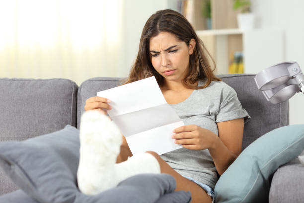 Worried disabled woman reading a letter Worried disabled woman reading a letter sitting on a couch in the living room at home unliked stock pictures, royalty-free photos & images