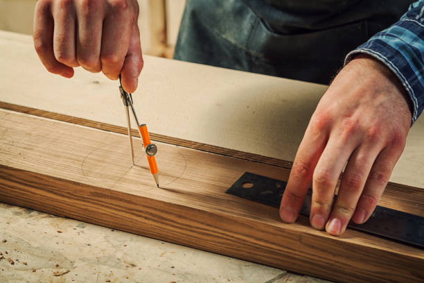 A close up of a male carpenter marks of a metal compass and a pencil on a wooden bar for making furniture.