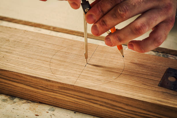 A close up of a male carpenter marks of a metal compass and a pencil on a wooden bar for making furniture.