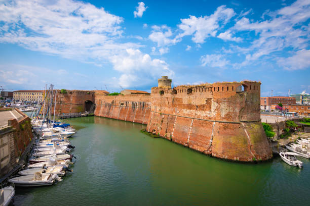 Old fortress of Livorno, Tuscany, Italy Fortezza Vecchia or old fort surrounded by green water and boats docked on the side.  Cruise ship in port at the background. Blue sky and white clouds. Bright and colorful image. Livorno, an old city port on the Ligurian Sea on the western coast of Tuscany, Italy. livorno stock pictures, royalty-free photos & images