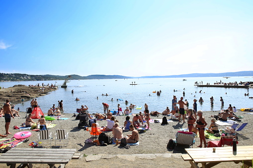 Oslo, Norway - July 22, 2018: Beach is located on Ulvoya island of the inner Oslofjord, just east of the city center. People relax sunbathing and swimming on beach on hot summer day.