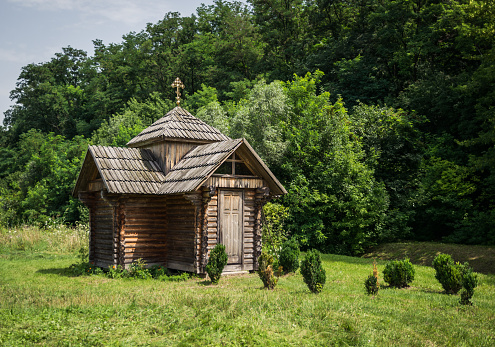 Summer picturesque countryside landscape. A small rustic wooden Orthodox chapel against the backdrop of a green meadow and forest