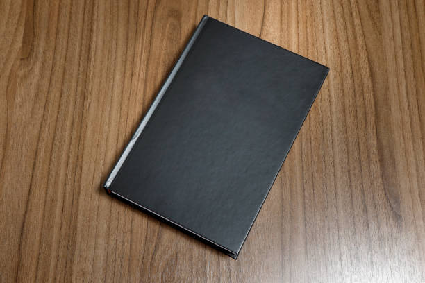 istock Black hardcover book on wooden surface - mock-up black book 1010610844