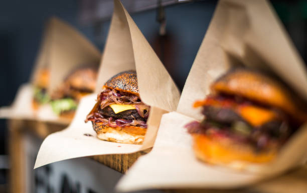 Fresh flame grilled burgers displayed in a row at food market Close up image of a selection of freshly flame grilled burgers in a row on a wooden counter at a London street food market. Each of the burgers has its own label, on which is written the contents of the burger. The burgers are sandwiched between glazed buns, and presented on beds of fresh green lettuce and stuffed with melted cheese and red onion. Horizontal colour image with copy space and beautiful bokeh background. burger close up stock pictures, royalty-free photos & images