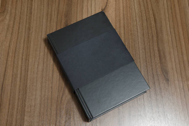istock Black hardcover book with protector on wooden surface - mock-up black book 1010614800
