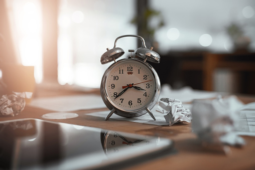 Still life shot of a clock and crumpled paper on a desk in an office at night