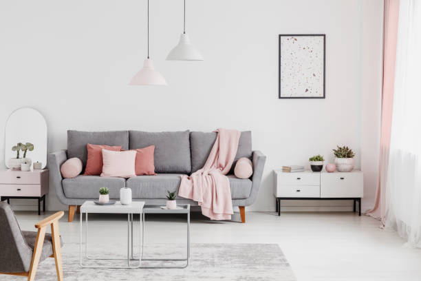 istock Pink blanket and cushions on grey settee in white flat interior with poster above cupboard. Real photo 1010630030