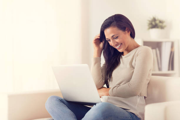 istock smiling woman using a laptop sitting on a couch 1010631222