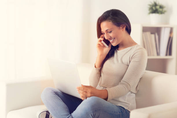 istock Happy Woman using a laptop and phone on a couch 1010631280