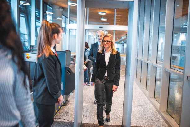 Passengers passing through metal detector at airport Staff looking at businesswoman and businessman passing through metal detector. Female is going through security check at airport. She is wearing formals. metal detector security stock pictures, royalty-free photos & images