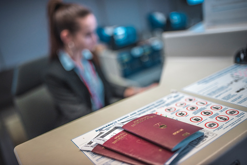 Passports and airplane tickets on counter. High angle view of airport check-in counter with staff in background. It is in focus.