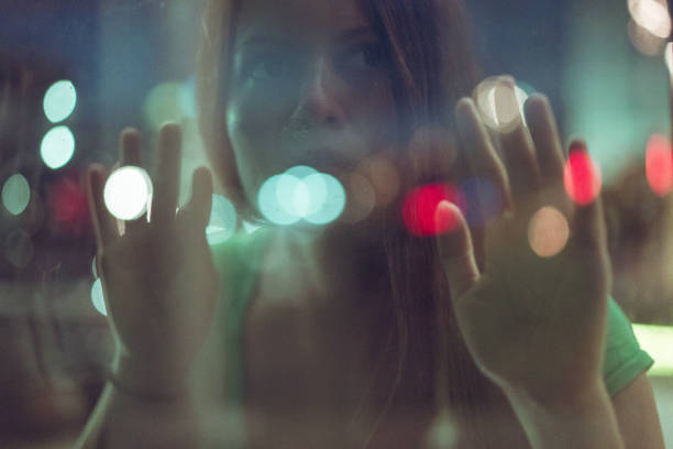 A teenage girl with red hair is sitting near the window. The girl looks into the camera and smiles lightly. Red-haired girl with black eyes. Delicate skin with freckles. Closeup portrait
