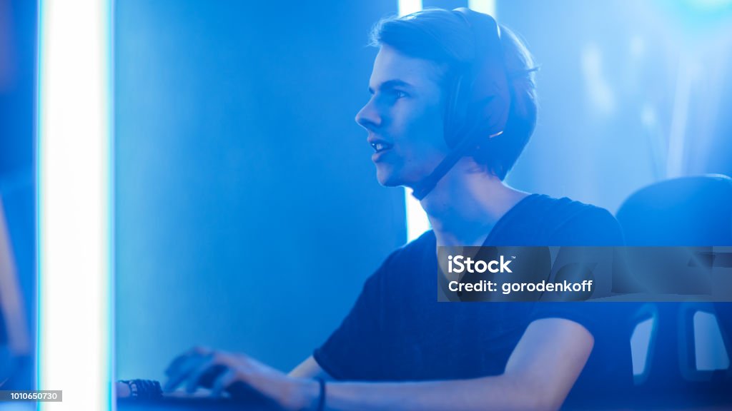 Shot of the Pro Gamer Playing in Video Games on His Personal Computer. Talking with His Team through Microphone on Headphones. Retro Neon Room. Video Game Stock Photo