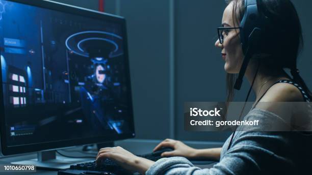 Shot Of The Beautiful Professional Gamer Girl Playing In Firstperson Shooter Online Video Game On Her Personal Computer Casual Cute Geek Wearing Glasses And Talking Into Headset In The Basement Gaming Club Stock Photo - Download Image Now