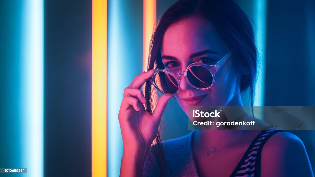 Portrait Shot of a Young Elegant Disco Girl Wearing Sunglasses. Room Lit in Retro / Retrowave Style with Neon and Pink Lights. Portrait Stock Photo