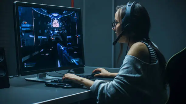 Photo of Beautiful Professional Gamer Girl Playing in First-Person Shooter Online Video Game on Her Personal Computer. Casual Cute Geek Girl Wearing Headset. In the Underground Gaming Club.