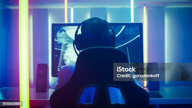 Back View Shot Of The Professional Gamer Playing In Firstperson Shooter Online Video Game On His Personal Computer Room Lit By Neon Lights In Retro Arcade Style Online Cyber Esport Internet Championship Stock Photo - Download Image Now