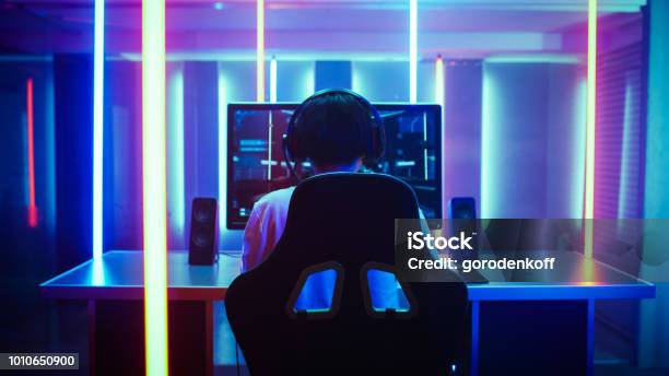 Back View Shot Of The Beautiful Professional Gamer Girl Putting On Headset And Starts Playing Online Video Game On Her Personal Computer Cute Casual Geek Girl Room Lit By Neon Lamps In Retro Arcade Style Stock Photo - Download Image Now