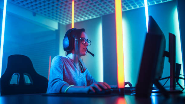 Low Angle Shot of the Beautiful Friendly Pro Gamer Girl Playing in Online Video Game and Streaming it, Wearing Headset Talks with Her Fans and Team into Headphones Microphone. Teenagers Having Fun. Background Cool Neon Retro Colors. bajo ángulo de tiro de la hermosa amable pro gamer chica jugando en juego de video en línea y streaming, usar auriculares conversaciones con su afición y equipo auriculares micrófono. adolescentes que se divierten. fondo fresco neón colores retro.