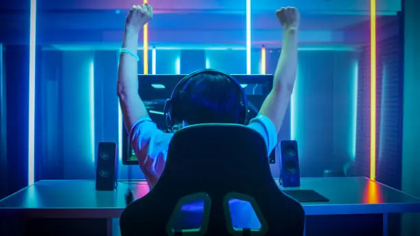 Photo of Professional Gamer Playing and Winning in First-Person Shooter Online Video Game on His Personal Computer. Footage Fade out into Bokeh. Room Lit by Neon Lights in Retro Arcade Style. Cyber Sport Championship.