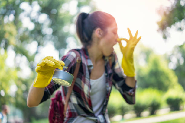 Young woman cleaning up smelly garbage in the park Young woman in the background pinching her nose while picking up stinking trash in the park holding nose stock pictures, royalty-free photos & images