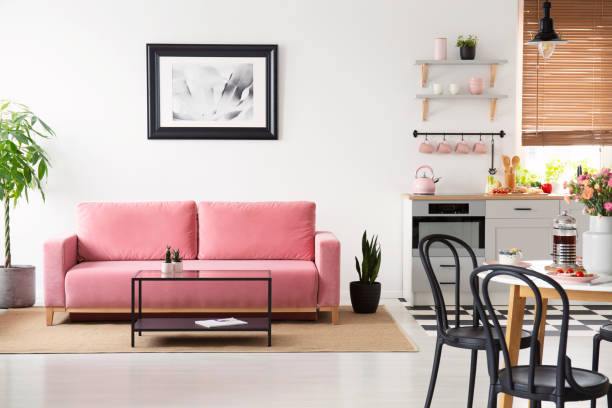 istock Poster above pink couch in white apartment interior with black chairs at table and kitchenette. Real photo 1010655852