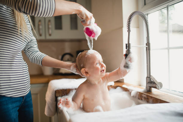 Mother Washes Child's Hair In The Sink A small baby enjoys his bubble bath in the sink as his mother washes his hair with bubbly water. kitchen sink photos stock pictures, royalty-free photos & images