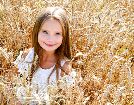 Smiling cute little girl on field of wheat outdoor