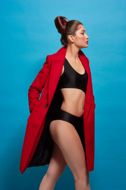 боковой вид движущийся модели с стройной фигурой в красном пальто, черном белье. - side view walking swimwear fashion model стоковые фото и изображения