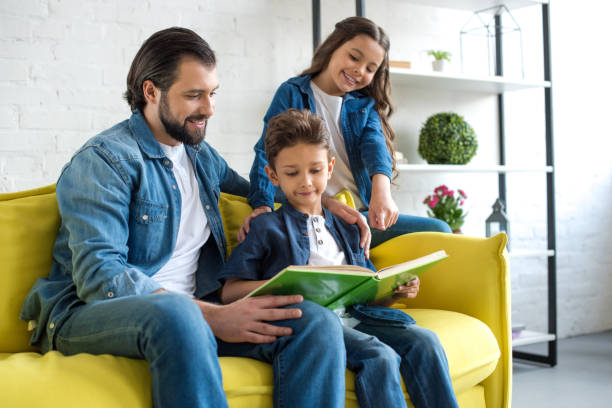istock smiling father with two kids reading book together while sitting on couch at home 1010697764