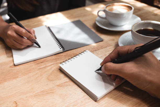 istock Closeup image of two business man writing down on a white blank notebook with coffee cup on wooden table in office 1010710110
