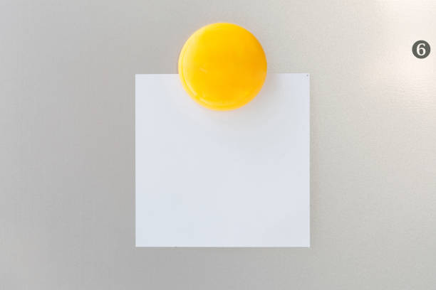 Yellow magnet paper clip on paper note on gray refrigerator background for input text.