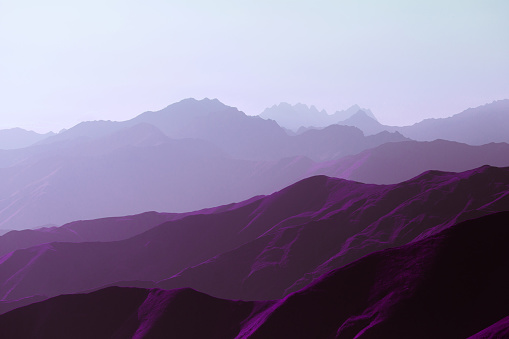 Surrealistic mountain landscape of purple hues. Panorama of rows of ridges against the background of the setting sun