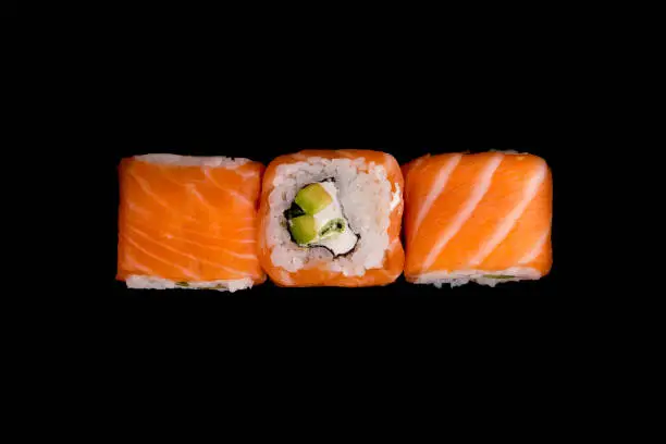 Japanese traditional food - sushi with avocado, rice, cottage cheese, salmon and green onion on the black background