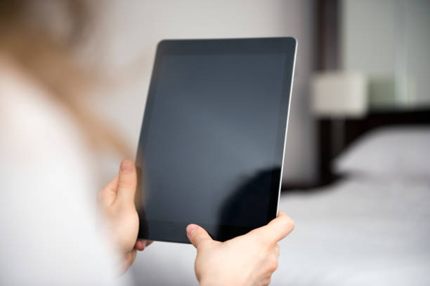 The photo was taken indoors in a domestic room. The photo was taken over the model's shoulder. The black device screen is left blank with copy space for your own website idea or text or photograph.