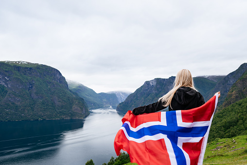Panorama of Aurlandsfjord. Tourist girl with the flag of Norway enjoys a beautiful view of the fjord and mountains