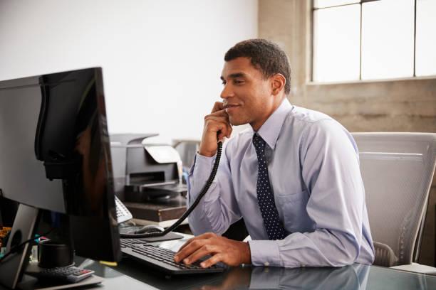 Businessman at an office desk using phone and computer