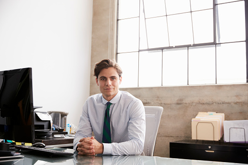 Young businessman sitting at office desk smiling to camera