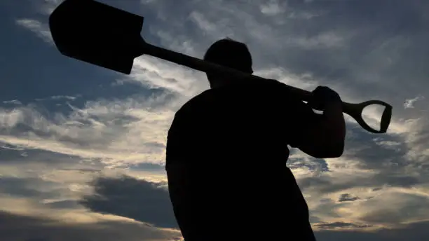 Silhouette of a man holding a shovel on his back