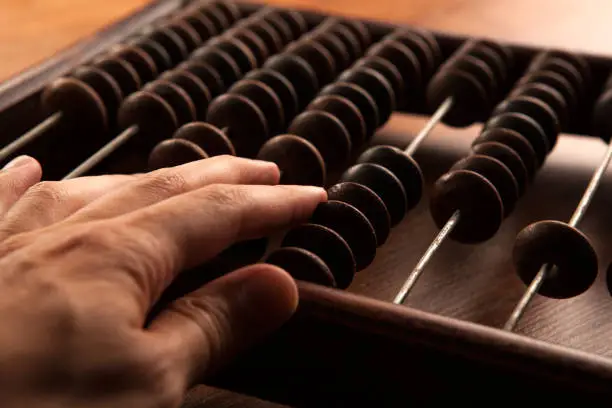 Photo of big antique abacus on a wooden table and the hand of man close up