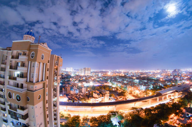 night cityscape of noida with skyscraper, monsoon clouds and moo Night aerial cityscape of a modern indian city with skyscrapers, residences, buildings, a busy street under a metro bridge. Shot on a monsoon night with clouds streaking across the sky and the moon peeping out hyderabad india stock pictures, royalty-free photos & images