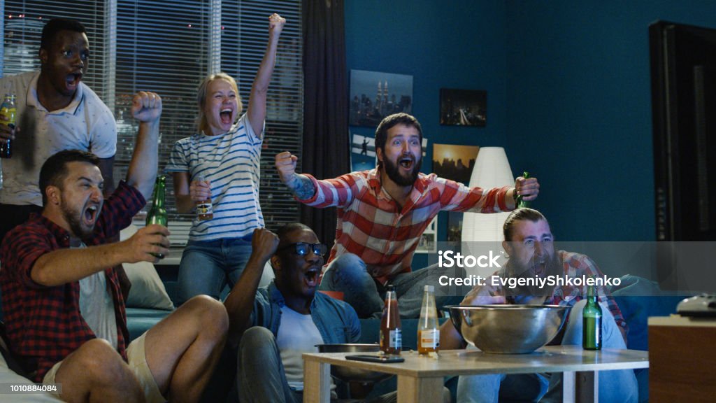 Excited fans cheering for sport team watching game View of diverse men and woman with beer and popcorn spilled cheering for winner team while watching sport game Watching Stock Photo