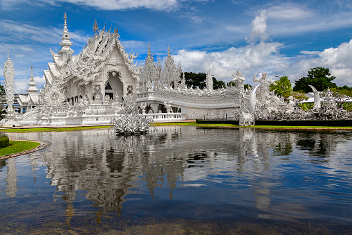 Chiang Rai, Thailand - June 23, 2018: White Temple known as Wat Rong Khun with its reflection in water, in Chiang Rai, Thailand.
