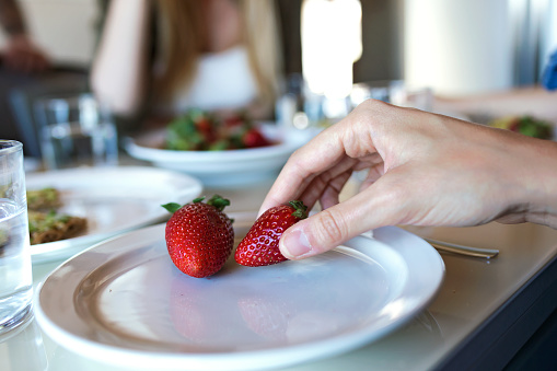 Close-up of woman's hand taking strawberries of a plate in the kitchen.