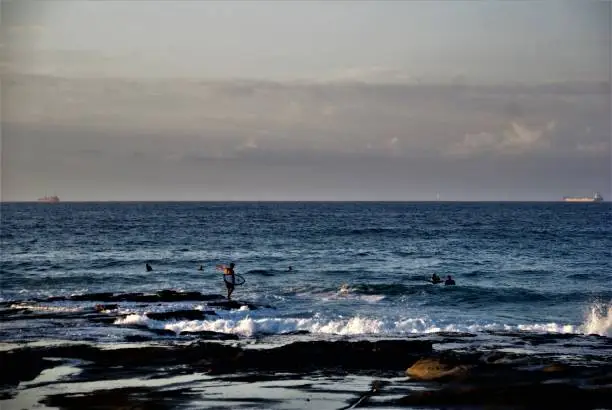 A surfer is trying to get into the water by crossing a serious amount of rocks.