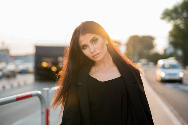 beautiful business womanwith pretty blue eyes across a street with sunset at background and trafic