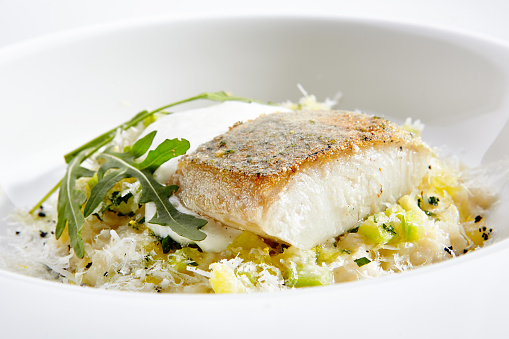 Close-up portrait of delicious pike perch with risotto. Fresh courgettes with some aerial espoume served with perfect taste. Isolated on white background